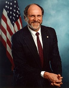 Three-quarter photographic portrait of a white man in his 50s, dressed in a suit and tie. He is balding but has a grayish beard, and he is wearing glasses.