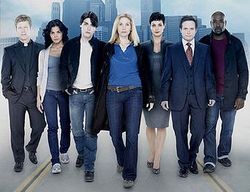 Seven cast members of V in a line with a city backdrop.