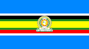 Nine horizontal strips coloured (from top to bottom): blue, white, black, green, yellow, green, red, white, then blue. The logo of the EAC is placed in the centre.