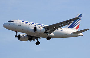 White jet aircraft coming into land, undercarriage fully extended. Under each wing is a turbofan engine