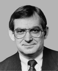 A dark-haired man in his fifties, wearing glasses and a suit, facing straight ahead