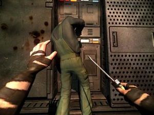 A pair of human arms with brown tape on them holding a screwdriver in the right hand. A man working on a machine, wearing a green jumpsuit and a black shirt, is in front of the arms with blood splatter on the wall to his left.