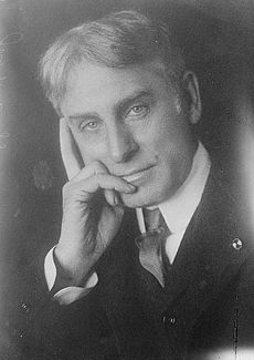 Middle-aged, thick-haired man wearing a suit and tie, gazing forward, his right hand touching the side of his face thoughtfully.