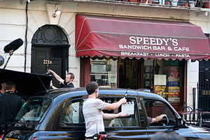 A street, with crew members looking towards a cafe and a house