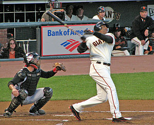 An African American man in a white baseball uniform with "GIANTS" on the chest takes a left-handed baseball swing as a catcher kneels behind him to receive the pitch.