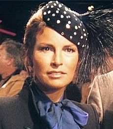 Welch in blue scarf and high-collared gray jacket, with polka-dot feathered cap