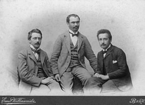 Three young men in suits with high white collars and bow ties, sitting.