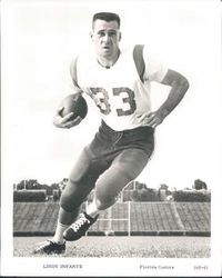 Photograph of Infante wearing a football uniform with pads (but no helmet) with a number 33 jersey cradling a football in his right arm