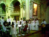 A choir and musicians dressed in white robes inside a church.