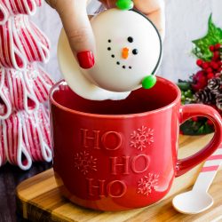 white chocolate snowman with candy ear muffsbeing placed inside a red mug