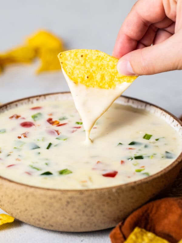 A bowl of queso blanco with a tortilla chip being dipped into it.