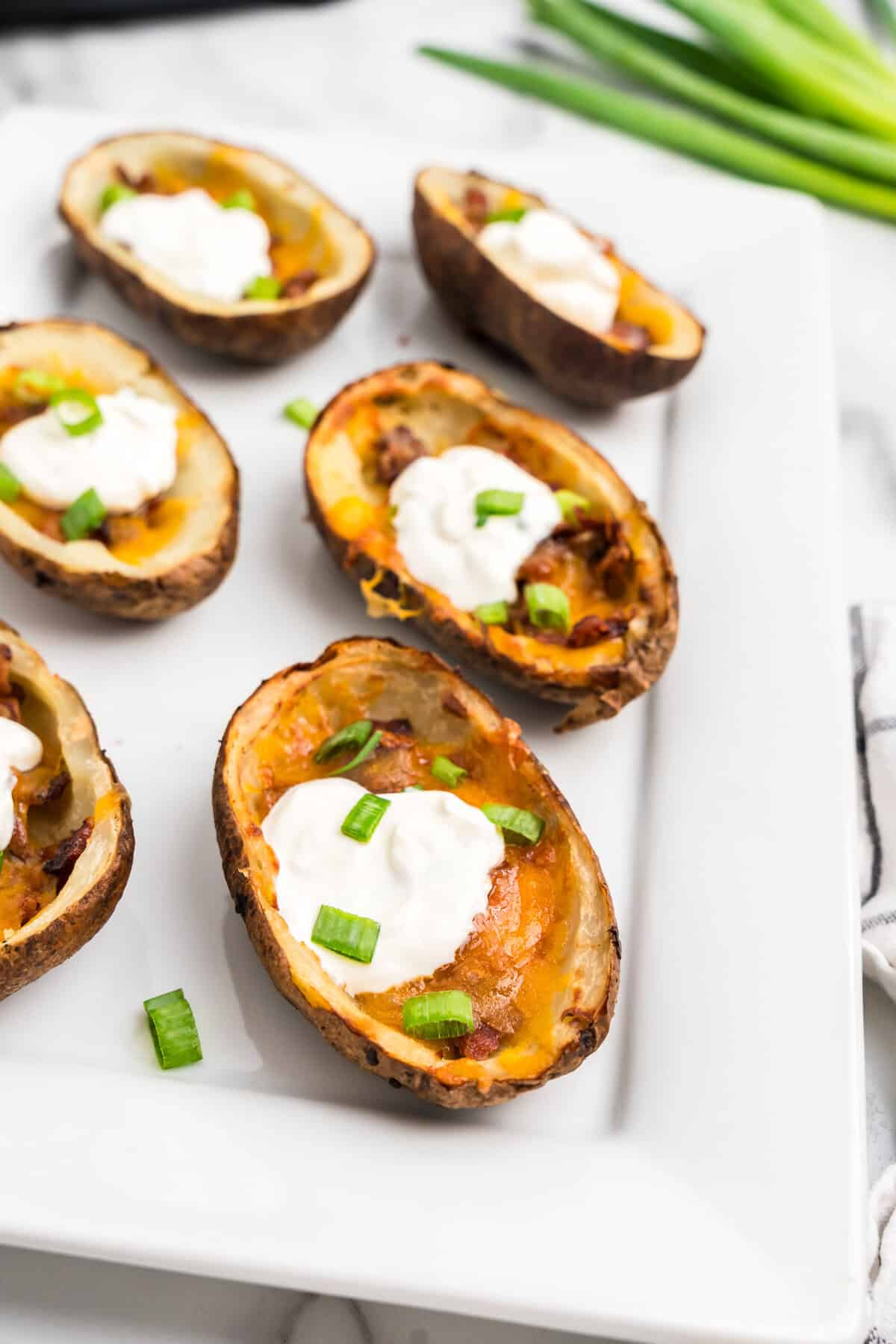 Air Fryer Potato Skins arranged on white serving plate topped with sour cream and chopped green onion