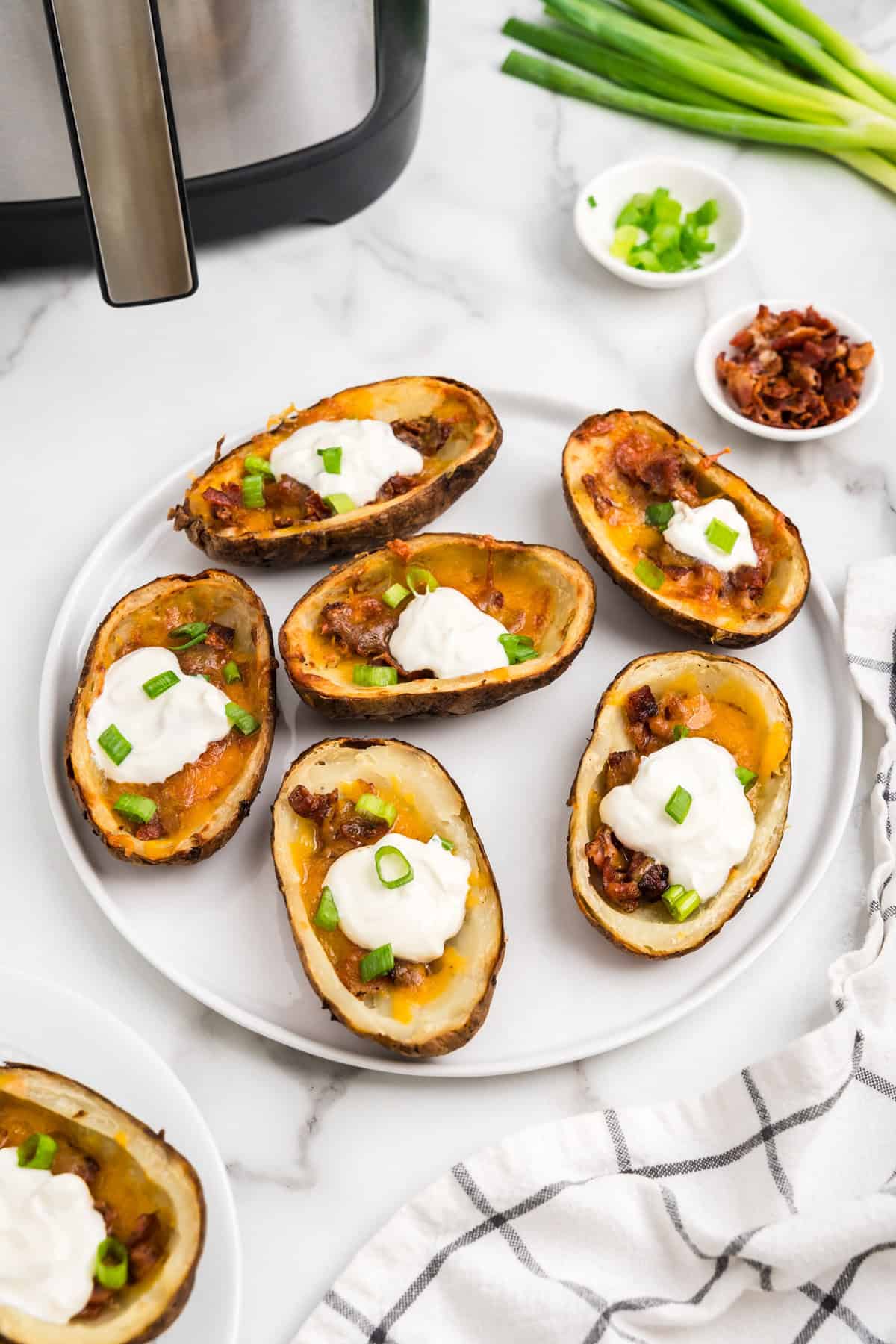 Air Fryer Potato Skins arranged on white serving plate topped with sour cream and chopped green onions