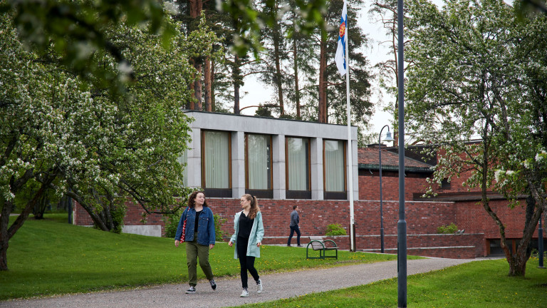 Opiskelijat kävelemässä vehreässä ympäristössä rakennuksen edustalla