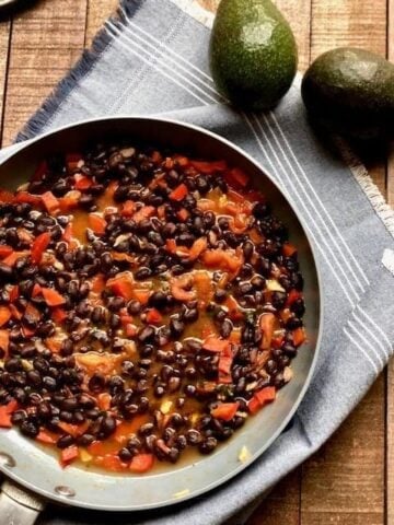 black beans in a pan with tomatoes sitting on a blue cloth