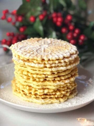 A stack of pizzelle with powdered sugar on top on a plate.