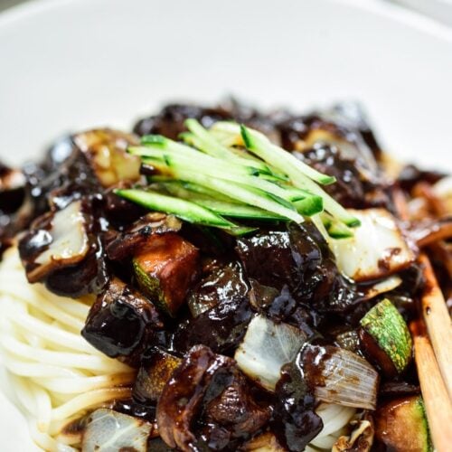 Korean noodles in a black bean sauce topped with cucumber matchsticks and served in a white bowl