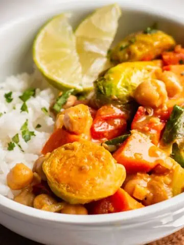 Vegan curry with a side of rice in a white bowl.