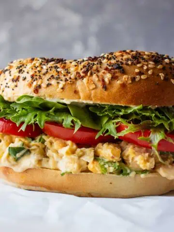 Vegan chickpea, bagel and tomato sandwich on a white parchment paper.