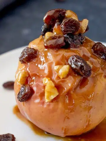 Baked apple with raisins, honey and walnuts on a white plate.