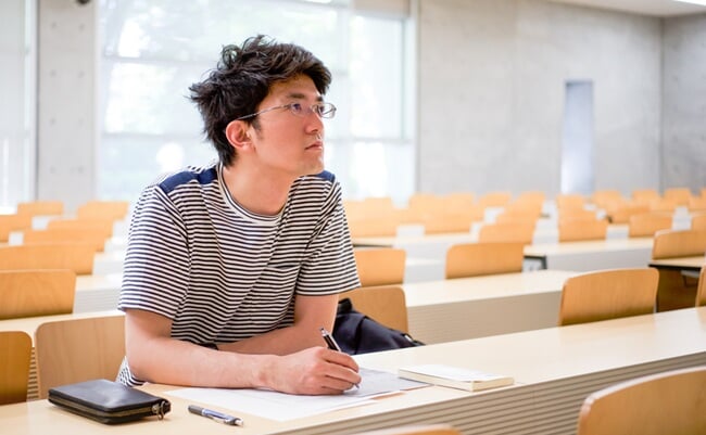 Student,Sitting,Reading,A,Book,And,Taking,Notes,In,Lecture