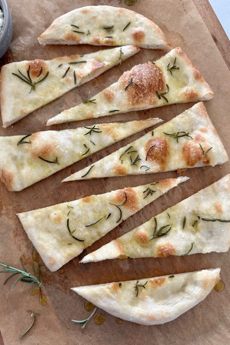 Sourdough pizza bianca sprinkled with rosemary and salt and sliced into wedges - served on a wooden board.