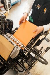 high angle view of a man putting orange paper into binding machine