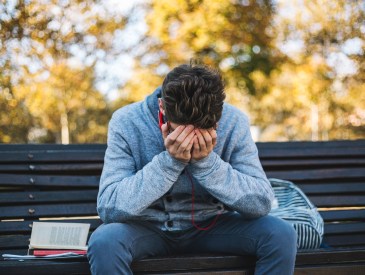 Teenager sits on a bench in the park and listen to music and learning for exame