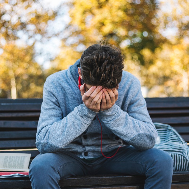 Teenager sits on a bench in the park and listen to music and learning for exame