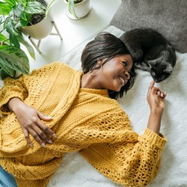 Smiling young woman lying with cat at home; nordstrom rack end of summer sale