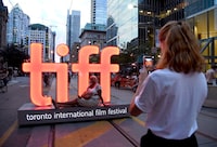 A volunteer takes a photo in front of a festival sign on day 1 of the Toronto International Film Festival on Thursday, Sept. 6, 2018, in Toronto. The Toronto International Film Festival returns to its full form after three years with in-person red carpets and a full slate of screenings, but many questions are swirling about the future of the film industry. THE CANADIAN PRESS/AP-Photo by Chris Pizzello/Invision/AP