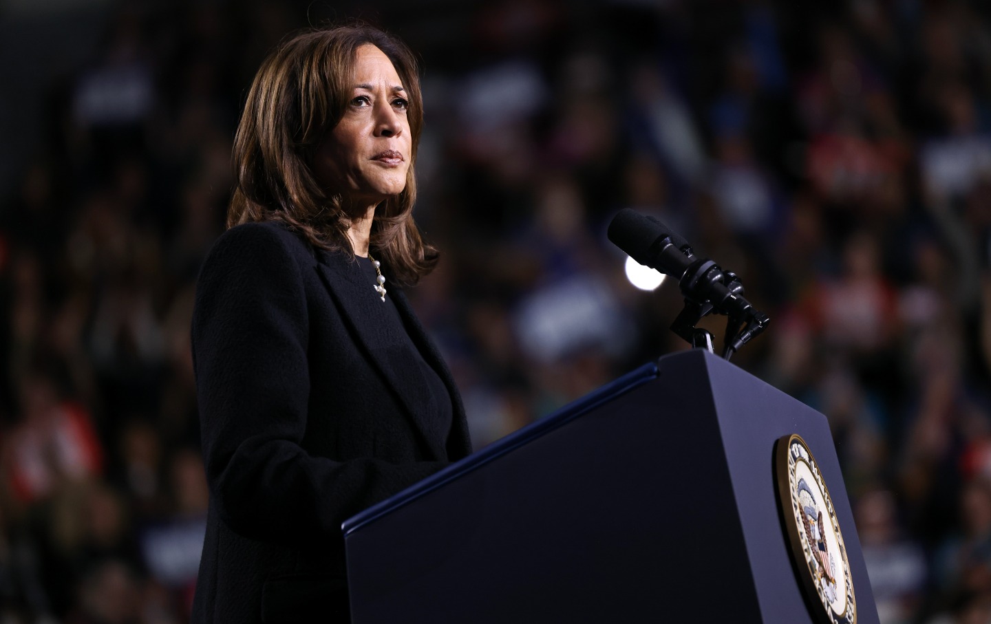 Vice President Kamala harris against a dark background, at a podium, looking reflective.