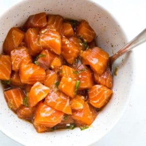 Bowl of salmon poke with a spoon in it on a white surface