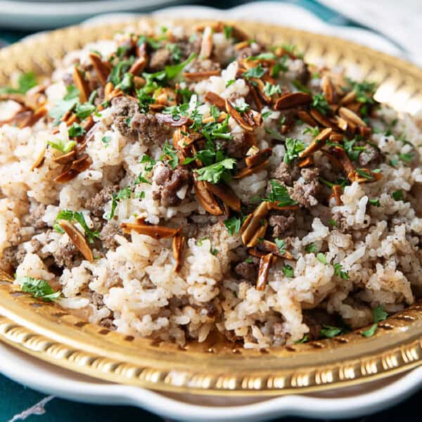 A close-up image of a plate filled with Hashweh rice, garnished with toasted pine nuts and fresh parsley.