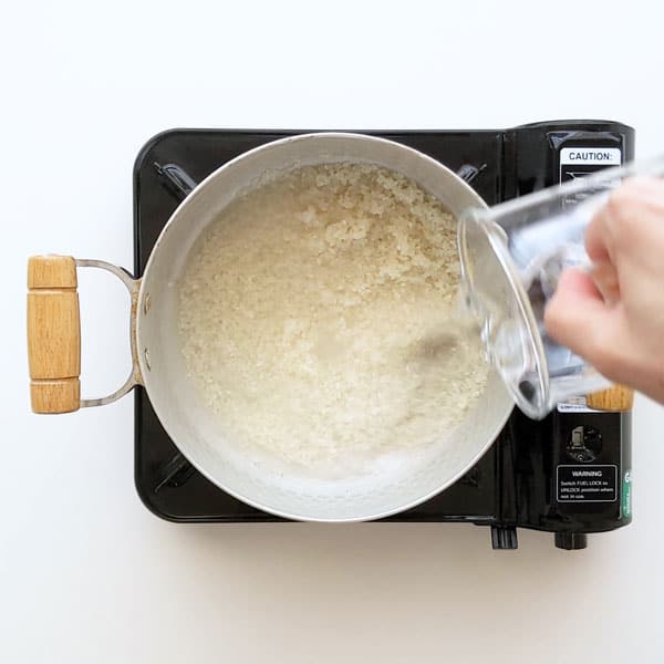 Pouring water over sushi rice in saucepan.