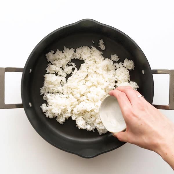 Pouring seasoned sushi vinegar over rice.