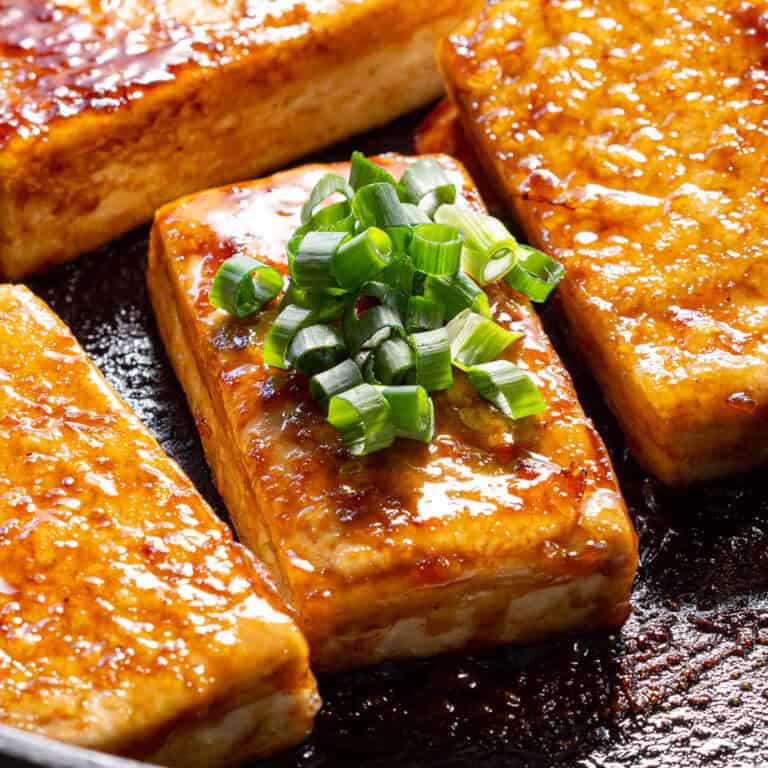 Super glossy teriyaki tofu with green onion in a frying pan.