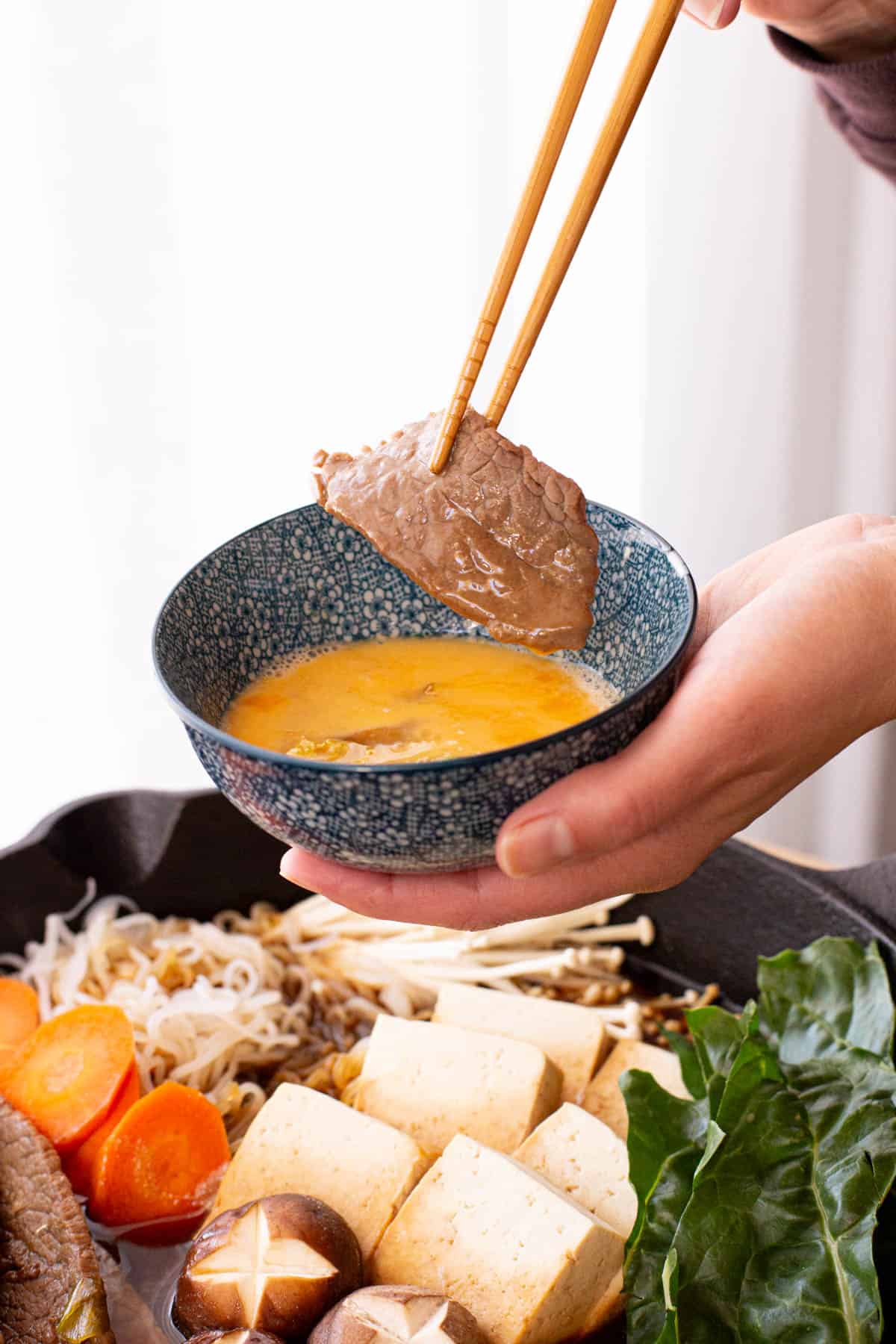 A piece of sukiyaki beef is dipped into egg.