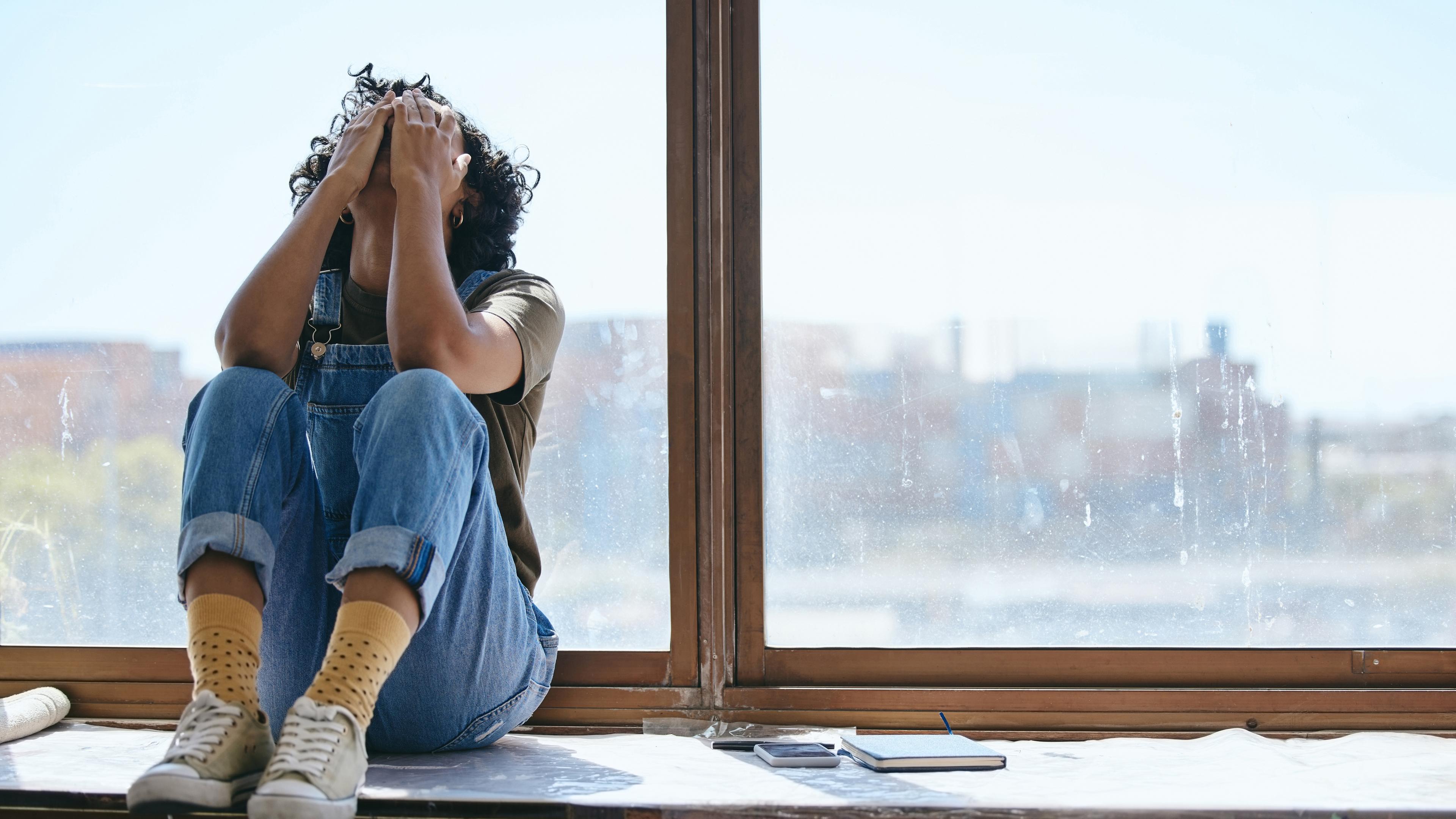 Junge Frau sitzt verzweifelt am Fenster