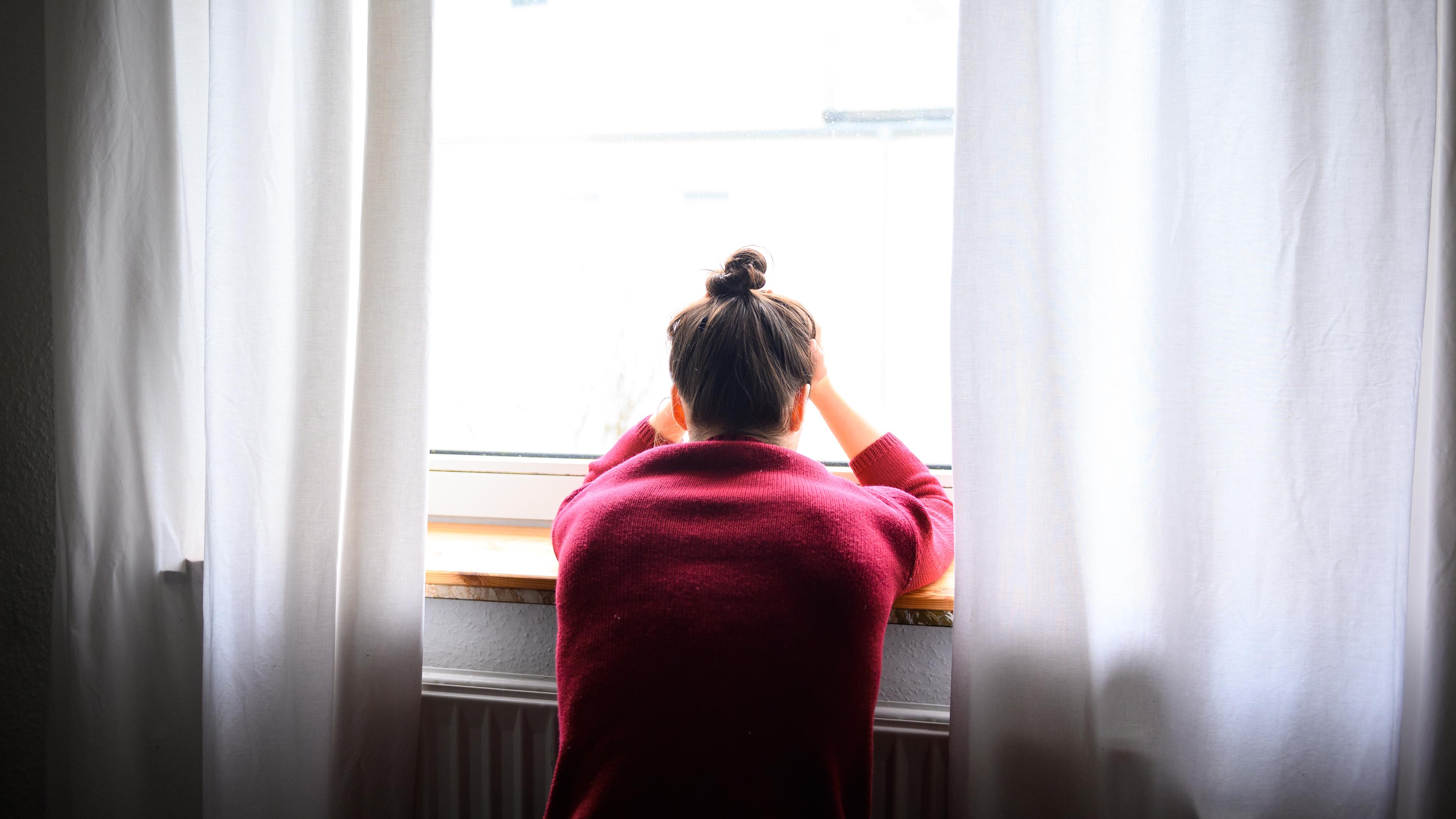 Eine Frau sitzt mit Kopf in den Händen am Fenster. Viele Menschen fühlen sich manchmal einsam