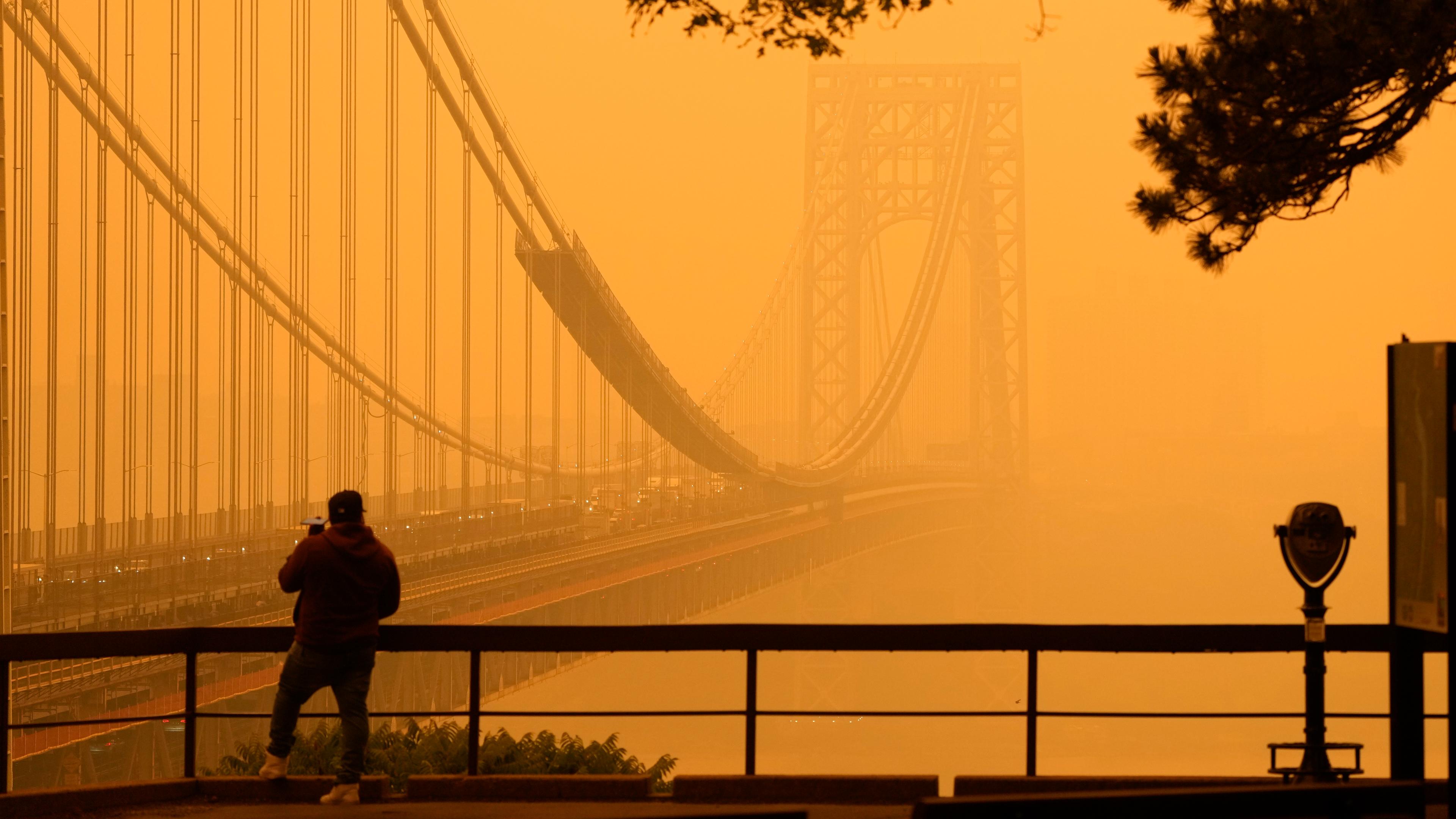 Ein Mann telefoniert, während er durch den Dunst vor der George Washington Bridge sieht.