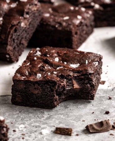 a square brownie with a bite taken out of it, with brownies stacked in the background