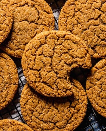 brown chewy-looking cookies stacked on a wire rack on a blue table