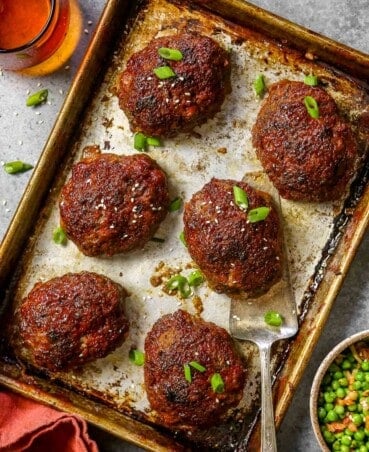 Mini meatloaf topped with sliced scallions on a baking sheet.